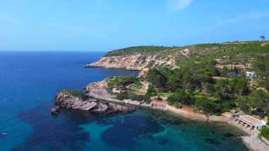 İspanya 'nın İbiza kentindeki lüks villanın havadan görünüşü, güneşli bir yaz gününde turkuaz su ve yelkenli yelkenli ile manzaralı bir körfez. İticileri ileri çalıştır 