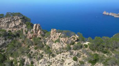 İspanya 'nın İbiza kentindeki kayalık bir uçurumda yürüyüş yapan bir grup turist, Akdeniz' in nefes kesici manzarasının tadını çıkarıyorlar. geniş yörünge görünümü dronu 