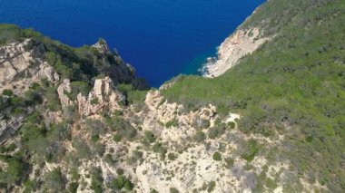 İspanya 'nın İbiza kentindeki kayalık bir uçurumda yürüyüş yapan bir grup turist, Akdeniz' in nefes kesici manzarasının tadını çıkarıyorlar. İHA panorama genel görüntüsü alçalıyor 