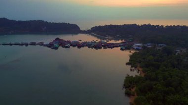 Tayland 'ın Koh Chang şehrinde günbatımında sakin suyu yansıtan geleneksel yüzen köyün hava manzarası. panorama genel görünüm dronu 