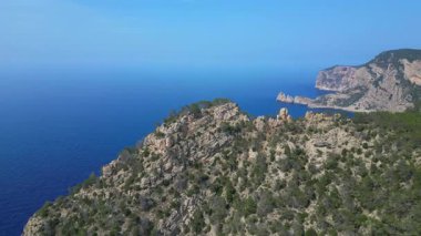 Kayalık kayalıkların ve yemyeşil bitki örtüsünün, İbiza kıyısındaki Akdeniz 'in engin genişliğiyle buluşması nefes kesici bir manzara. geniş yörünge görünümü dronu 