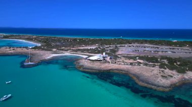 İspanya 'nın Formentera kentindeki bir sahil barının yakınındaki turkuaz sularda demirleyen yelkenliler nefes kesici bir hava perspektifi sunuyorlar. panorama yörünge dronu 