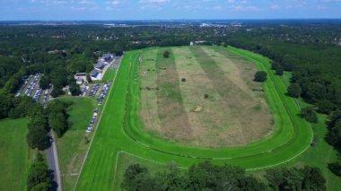 Almanya 'da bir ormanın yakınındaki at yarışı pistinin havadan görünüşü, park yeri görünür. İHA alçalıyor 