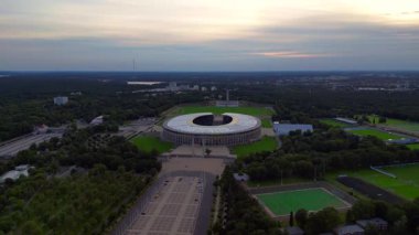 Günbatımında Olympiastadion Berlin 'in havadan görünüşü çan kulesini, park alanlarını ve şehrin ufuk çizgisini gösteriyor. geniş yörünge görünümü dronu 