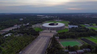 Günbatımında Olympiastadion Berlin 'in havadan görünüşü çan kulesini, park alanlarını ve şehrin ufuk çizgisini gösteriyor. geniş yörünge görünümü dronu 