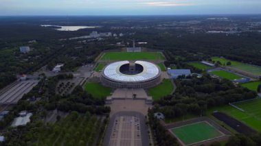 Günbatımında Olympiastadion Berlin 'in havadan görünüşü çan kulesini, park alanlarını ve şehrin ufuk çizgisini gösteriyor. Yukarıdan aşağıya doğru uçur 