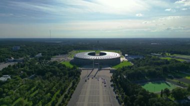 Güneşli yaz gününde Olympiastadion Berlin 'in hava manzarası çevredeki ağaçları ve otoparkı gösteriyor. Ters İHA uçuşu 