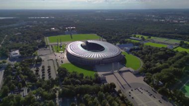 Güneşli yaz gününde Olympiastadion Berlin 'in hava manzarası çevredeki ağaçları ve otoparkı gösteriyor. İticileri ileri çalıştır 