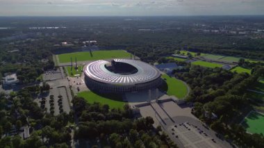 Güneşli yaz gününde Olympiastadion Berlin 'in hava manzarası çevredeki ağaçları ve otoparkı gösteriyor. Yukarıdan aşağıya doğru uçur 