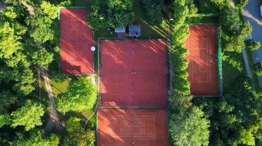 Yoğun bir ormanın içine yerleştirilmiş çok sayıda tenis kortunun havadan görünüşü şehrin kalbine huzurlu bir kaçış sağlıyor. dikey kuş bakışı dron 