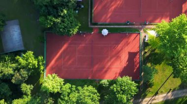 Güneşli bir günde kil kortlarda tenis oynayan insanların hava görüntüsü. dikey kuşların gözünden drone kameralar aşağıya bakıyor. uçuş üstü insansız hava aracı 
