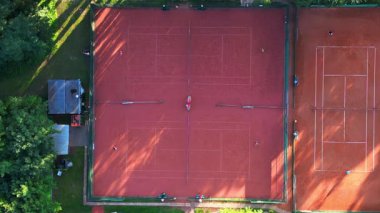 Güneşli bir günde kil kortlarda tenis oynayan insanların hava görüntüsü. dikey kuşların gözünden drone kameralar aşağıya bakıyor. statik üç ayaklı insansız hava aracı 