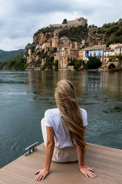 stock image Back photography of caucasian woman with long blonde hair sitting in the pier looking the village in front of the river. High quality photo