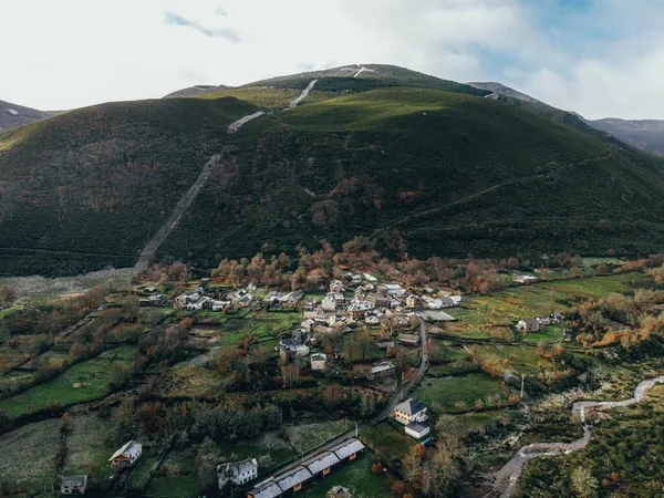 Drone view of a village surrounded by green mountains and a river in a cloudy day