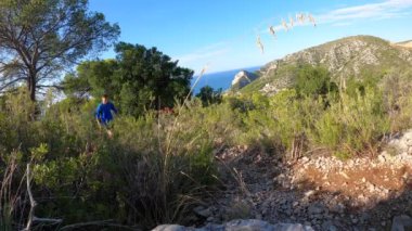 Young man with blue sport t-shirt hiking and exploring forest area near the sea. 