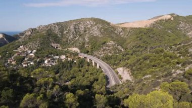 Drone view of highway crossing mountains with tunnels and blue sea on clear horizon. Garraf, Spain