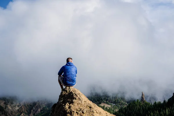 Loneliness rearview of man with blue jacket on a rock with the amazing view of Roque Nublo natural park in Gran Canaria, Canary Islands