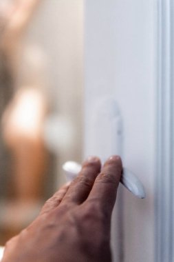 Close-up of a hand entering in the bathroom and defocused woman has a shower in the background.