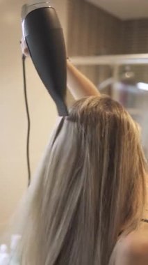4k film vertical unrecognizable blonde woman with wet hair drying her hair with dryer in modern bathroom in front of mirror