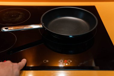Close-up of empty frying pan with hand switching the induction in orange kitchen