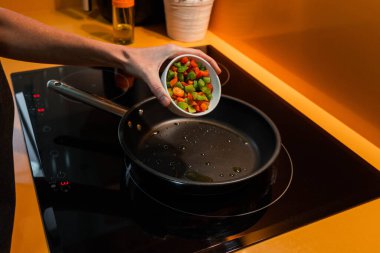 Unrecognizable person throwing vegetables in a frying pan. Orange kitchen