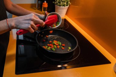 Unrecognizable person throwing vegetables in a frying pan. Orange kitchen