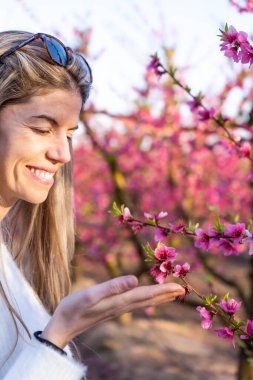 Aitona 'da bir tarlada gülümseyen sarışın kadın. Baharda güneş gözlüklü pembe çiçekler.