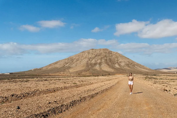 Blonde woman in awesome landscape of mountain and a sky cover by clouds. Fuerteventura, canary islands