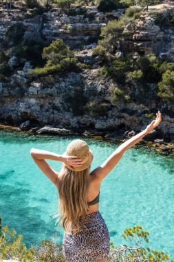 Kaliforniya pi, Mallorca ve Balear Adaları 'nda uzun sarı saçlı bir kadın. Turkuaz su kayalarla çevrili.
