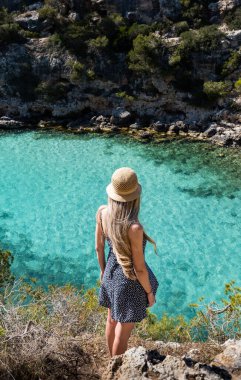 Kaliforniya pi, Mallorca ve Balear Adaları 'nda uzun sarı saçlı bir kadın. Turkuaz su kayalarla çevrili.