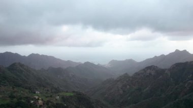 İHA görüntüsünün 4K görüntüsü. Yoğun sis manzarası dağları ve ortasında evler olan bir yol. Tenerife, Kanarya Adaları