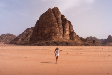 Sarışın bir turist, kum tepecikleri ve Ürdün 'ün Wadi Rum çölünde Muhteşem Kaya' da yürüyor. Seyahat yerleri