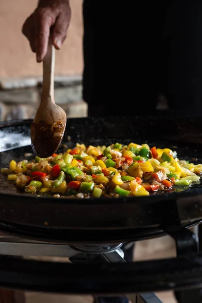 Paella 'yı İspanya tarifinden hazırlayan yaşlı adam büyük bir tavada ahşap kaşıkla sebze kızartıyor.