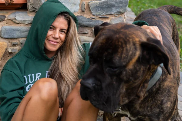 Kapüşonlu sarışın kadın ve köpeği Presa Canario veya Dogo açık havada evdeler.