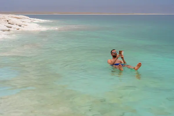 Yüzen Ölüm Denizi 'nde banyo yaparken kitap okuyan turist, Jordan.