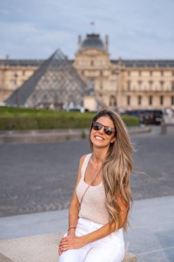Paris 'teki Louvre Müzesi' nin girişinde gülümseyen bir turistin dikey fotoğrafı.