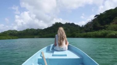Panama 'da huzurlu bir gölde bir teknenin kenarında oturan sarışın genç bir kadının arka görüntüsü.