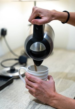 Dişi ellerin dikey yakın çekimi su dolduruyor ve bir bardağa elektrikli su dolduruyor.