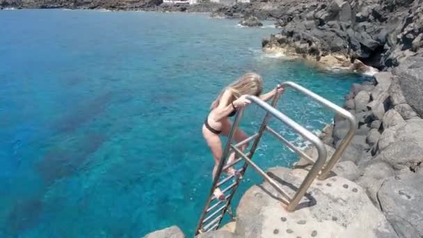 一个金发碧眼的美女从岩石直奔大海的楼梯上下来的视频 — 图库视频影像