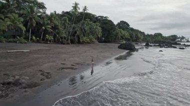Sarışın bir kadının vahşi bir tropik plajda tek başına yürüdüğünü gösteren hava aracı videosu. Nuqui bölgesi, Kolombiya