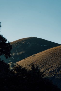 Arka planda mavi gökyüzü olan bir dağ sırası. Dağlar ağaçlarla örtülmüş, gökyüzü ise berrak.