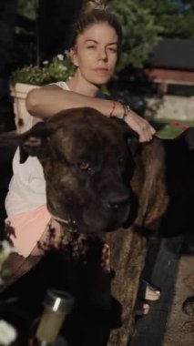 Huzurlu bir bahçede, bir kadın büyük sert kanarya köpeğine sevgiyle sarılır, dostluk ve sıcaklıkla dolu güzel ve sakin bir öğleden sonranın tadını çıkarır..