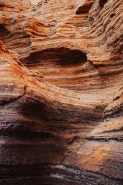 Görüntü, ortasında bir delik olan kayalık bir uçurum. Renkler sıcak ve topraksı, doğal ve engebeli bir manzara izlenimi veriyor. Kayaların dokusu pürüzlü ve pürüzlü.