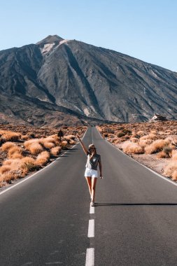 Kadın, engebeli dağlarla çevrili düz ve boş bir yolda güvenle yürüyor. Tenerife 'de çay ve kuru bitki örtüsü, manzaranın huzurunun tadını çıkarıyor..