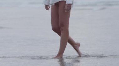 Gün batımında plajda yalın ayak yürüyen bir insan, sakin dalgaların ve sakin bir gecenin atmosferinin tadını çıkarıyor..