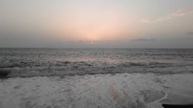 Dalgaların drone görüntüsü, güneş ufukta batarken sakin bir plaja yuvarlanıyor ve sakin bir atmosfer yaratıyor..