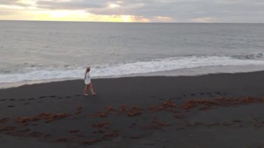 Bir kadın güneş batarken sakin bir kumsalda geziniyor, Lanzarote 'de gökyüzünü ılık renklerle boyuyor.