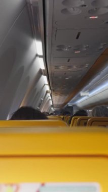 Yolcuların dikey videosu, sarı koltuklarla çevrili, rahat ve aydınlık bir uçakta, uçuşun keyfini çıkartıyor..