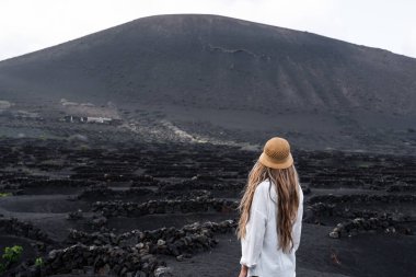 La Geria 'da bir kadının arkadan görünüşü, üzüm bağı şarap manzarası Lanzarote' de dairesel taş tepecikleriyle dolu volkanik arazi..