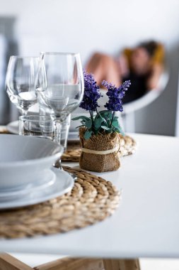 İyi düzenlenmiş bir yemek masasında cam eşyalar, tabaklar ve çiçekli bir süs eşyası bulunur..
